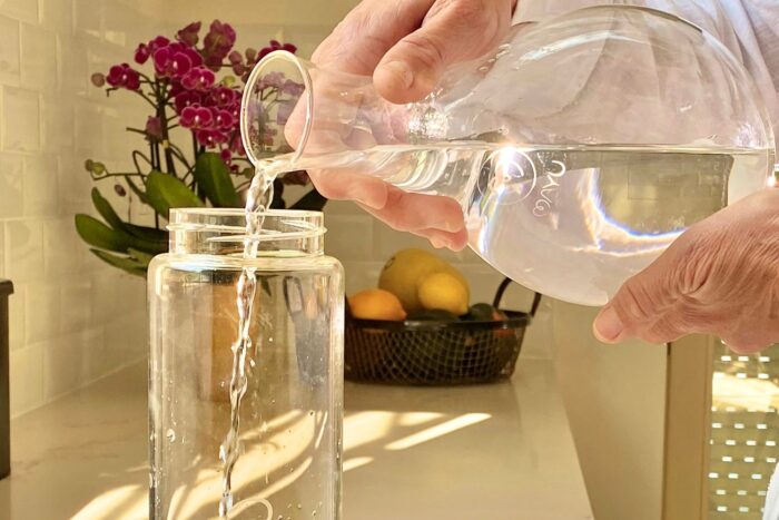 Wasser aus der MAYU Swirl Karaffe wird in eine MAYU Glasflasche umgefüllt